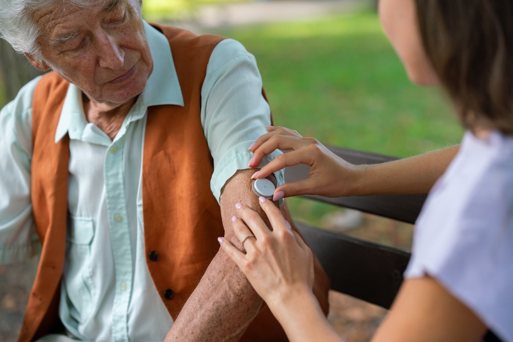 Caregiver helping senior diabetic man to apply continuous glucose monitor- To Monitor Endocrine Hormonal Changes.